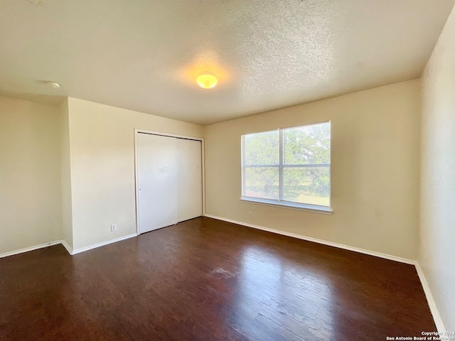 unfurnished bedroom with a textured ceiling, dark wood-type flooring, and a closet