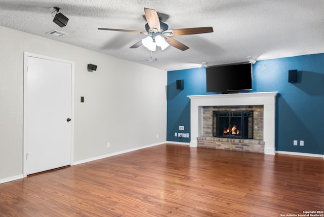 unfurnished living room with ceiling fan, wood-type flooring, a textured ceiling, and a brick fireplace