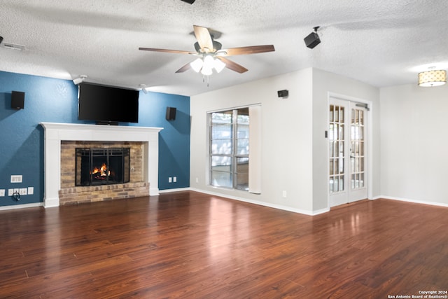 unfurnished living room featuring ceiling fan, french doors, a brick fireplace, dark hardwood / wood-style floors, and a textured ceiling