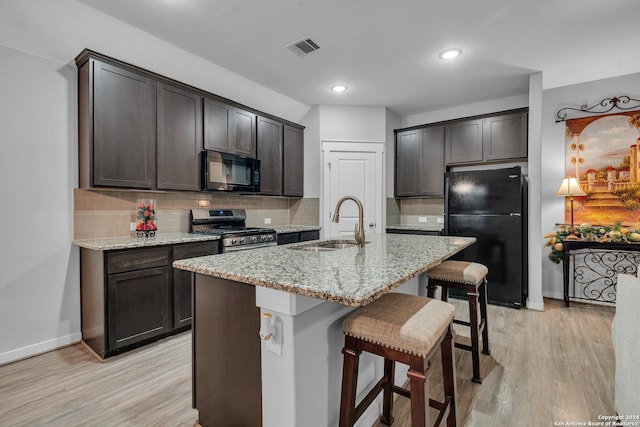 kitchen featuring light wood-type flooring, an island with sink, tasteful backsplash, and black appliances