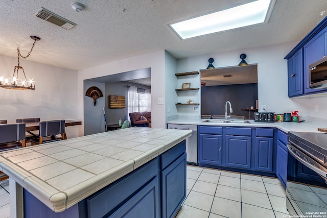 kitchen featuring stainless steel appliances, blue cabinets, sink, decorative light fixtures, and tile counters