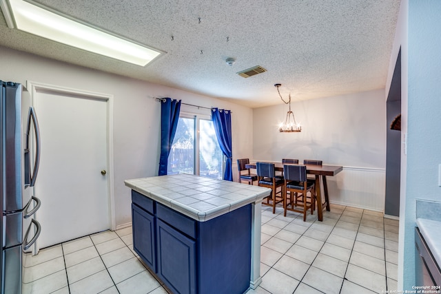 kitchen featuring appliances with stainless steel finishes, a textured ceiling, tile countertops, a chandelier, and hanging light fixtures