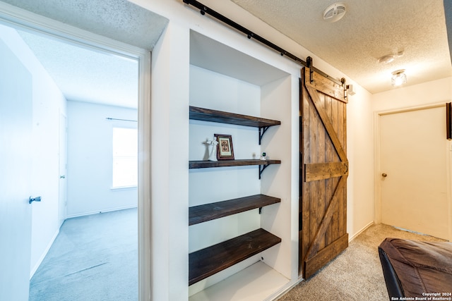 corridor featuring a textured ceiling, a barn door, and light carpet