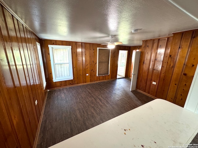 unfurnished bedroom with a textured ceiling, wooden walls, and dark wood-type flooring