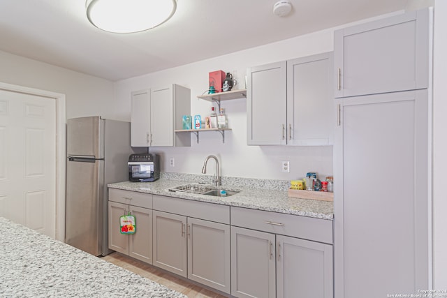 kitchen featuring light stone countertops, gray cabinetry, sink, light hardwood / wood-style floors, and stainless steel refrigerator