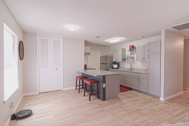 kitchen with gray cabinetry, a breakfast bar, sink, light hardwood / wood-style flooring, and stainless steel refrigerator