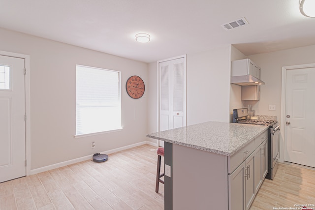 kitchen featuring a kitchen bar, light stone countertops, light hardwood / wood-style floors, gray cabinetry, and stainless steel stove