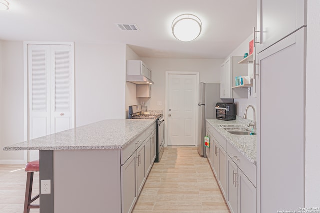 kitchen with sink, a breakfast bar area, light hardwood / wood-style floors, light stone counters, and stainless steel appliances