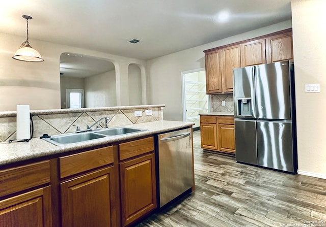 kitchen with sink, stainless steel appliances, tasteful backsplash, decorative light fixtures, and hardwood / wood-style flooring