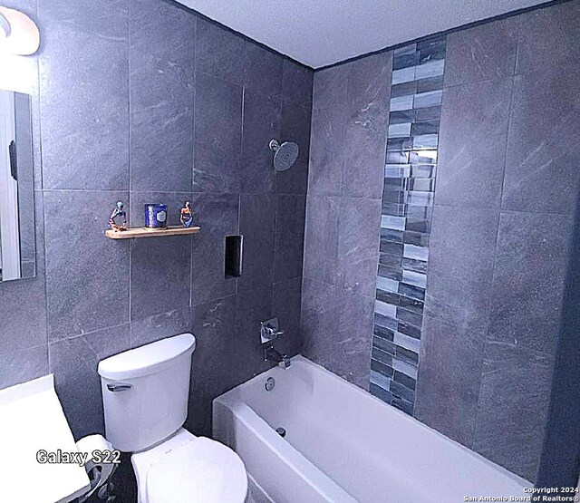 full bathroom featuring tiled shower / bath, vanity, toilet, and tile walls