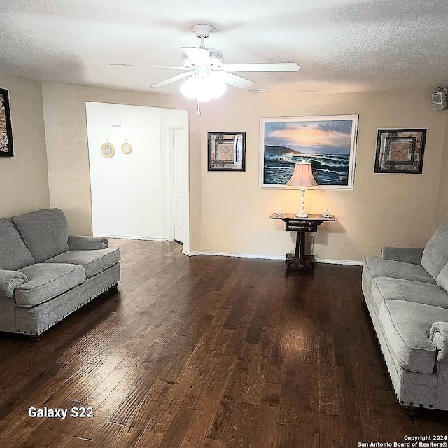 living room featuring ceiling fan, dark wood-type flooring, and a textured ceiling