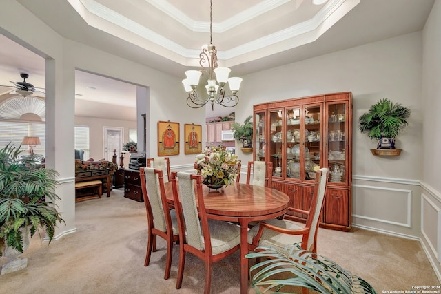 carpeted dining room with ceiling fan with notable chandelier, a raised ceiling, and crown molding