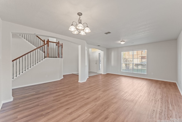 unfurnished living room featuring a textured ceiling, hardwood / wood-style flooring, and an inviting chandelier