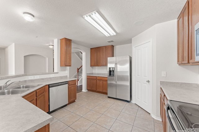 kitchen with a textured ceiling, sink, light tile patterned floors, and stainless steel appliances