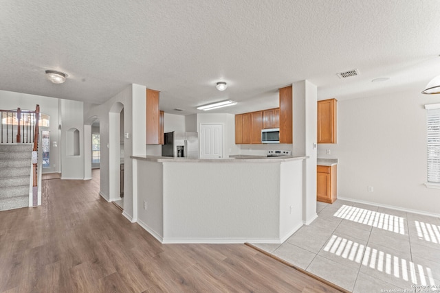 kitchen featuring kitchen peninsula, a textured ceiling, stainless steel appliances, and light hardwood / wood-style floors