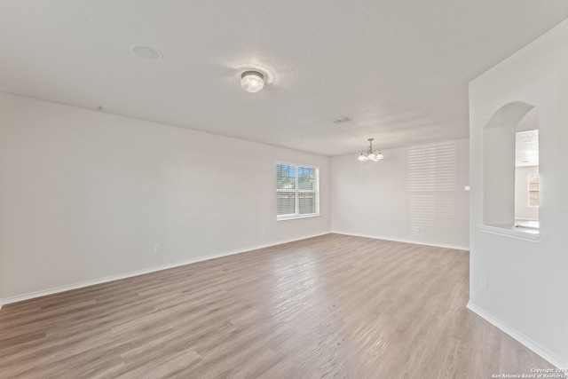 empty room with a textured ceiling, light hardwood / wood-style floors, and a notable chandelier