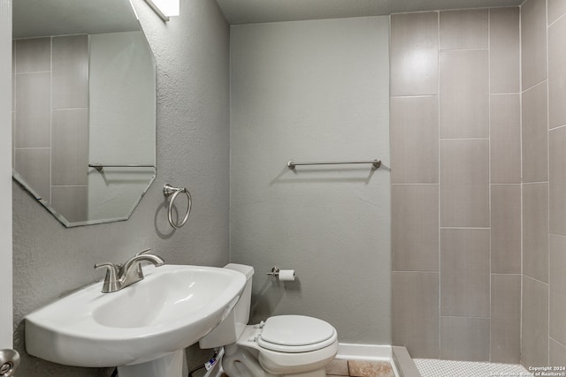 bathroom with a tile shower, toilet, and sink