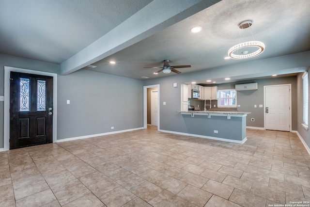 interior space featuring a textured ceiling, a wall unit AC, beam ceiling, and ceiling fan with notable chandelier