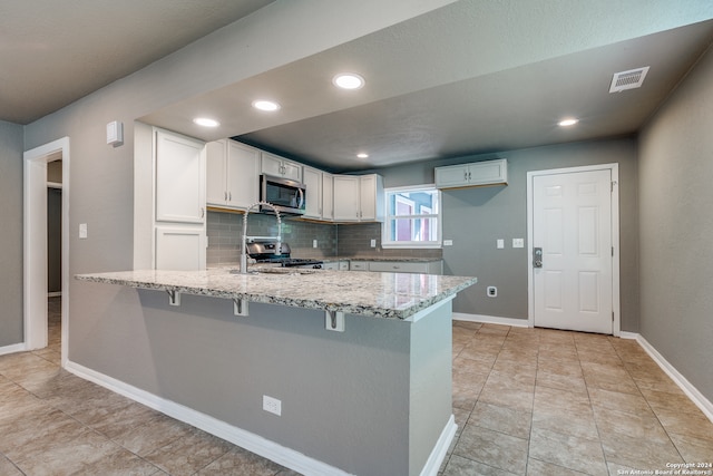 kitchen with white cabinets, light stone countertops, tasteful backsplash, a kitchen bar, and stainless steel appliances