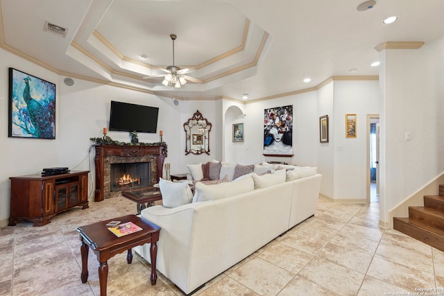 living room with a fireplace, a tray ceiling, ceiling fan, and ornamental molding