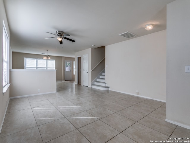 tiled empty room featuring ceiling fan with notable chandelier