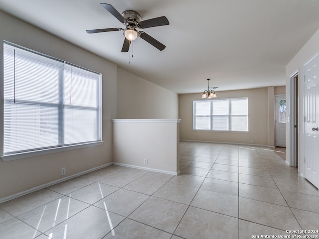 tiled empty room featuring ceiling fan with notable chandelier