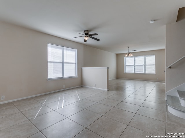 tiled empty room with ceiling fan with notable chandelier