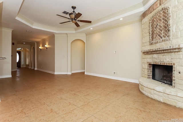 unfurnished living room featuring ceiling fan, a stone fireplace, ornamental molding, and a tray ceiling