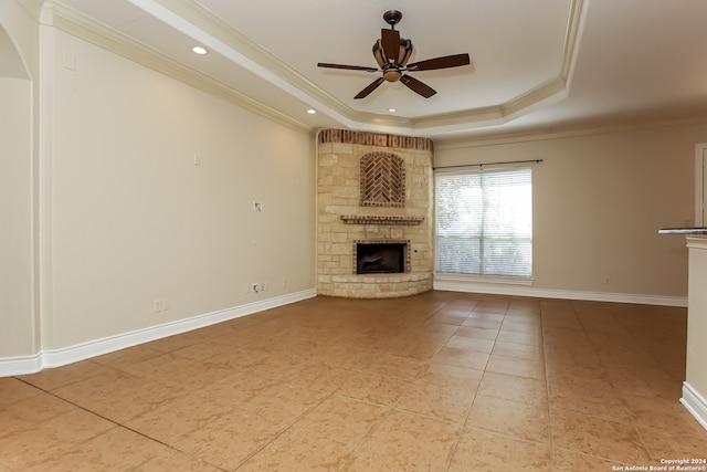 unfurnished living room featuring a stone fireplace, crown molding, tile patterned flooring, ceiling fan, and a tray ceiling