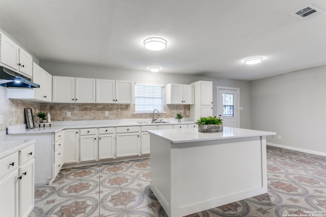 kitchen featuring backsplash, white cabinetry, a kitchen island, and sink