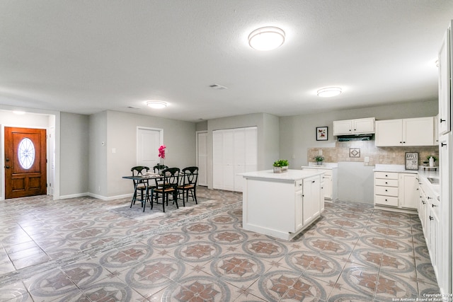 kitchen with a textured ceiling, a kitchen island, white cabinetry, and backsplash