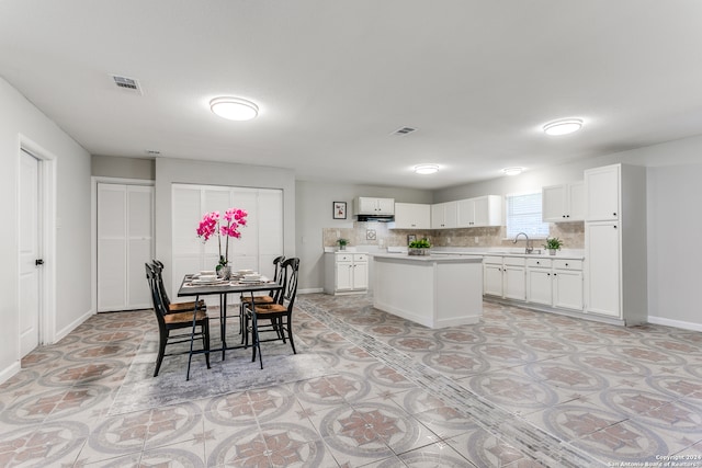 kitchen with decorative backsplash, a center island, white cabinets, and sink