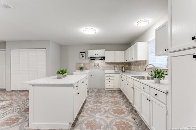 kitchen with white cabinets, decorative backsplash, a kitchen island, and sink