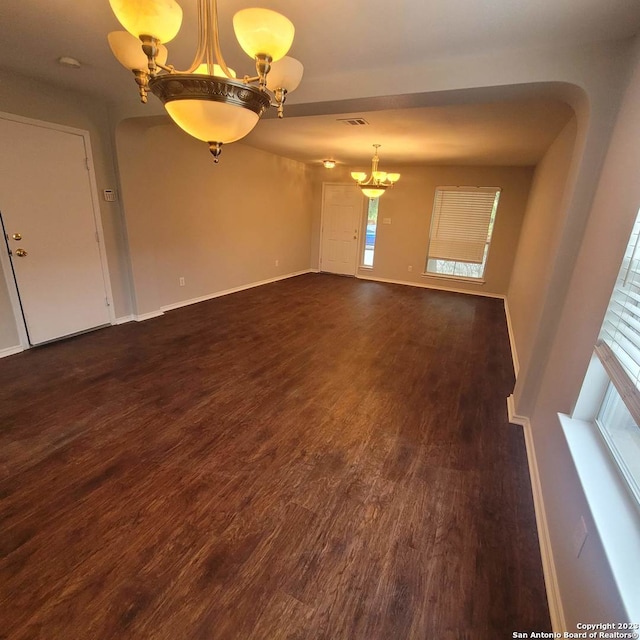 spare room featuring dark wood-type flooring, a healthy amount of sunlight, and an inviting chandelier