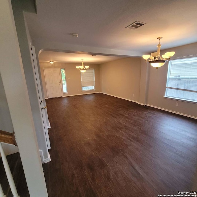 unfurnished living room with dark wood-type flooring, a healthy amount of sunlight, and an inviting chandelier