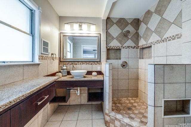 bathroom with a tile shower, tile patterned flooring, vanity, and tile walls