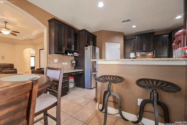 kitchen with stainless steel fridge, backsplash, light stone counters, ceiling fan, and light tile patterned flooring