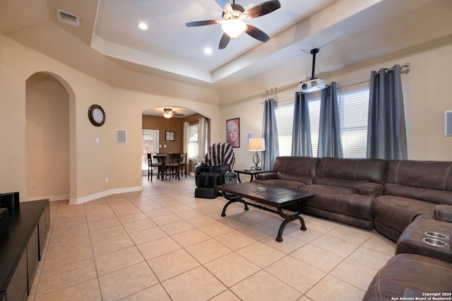 living room featuring a raised ceiling, ceiling fan, and light tile patterned flooring