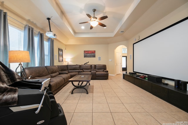 tiled home theater room with ceiling fan and a raised ceiling