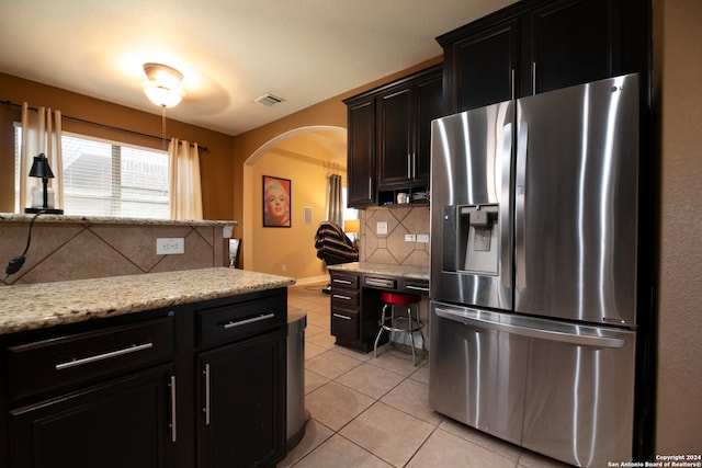 kitchen with light tile patterned flooring, light stone countertops, stainless steel fridge with ice dispenser, and tasteful backsplash