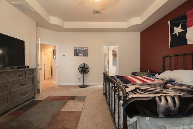 carpeted bedroom with a tray ceiling, ensuite bath, and ceiling fan