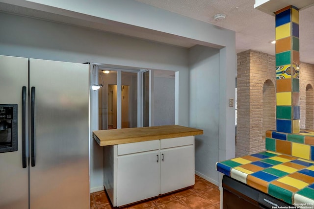 kitchen featuring white cabinets, light tile patterned floors, a textured ceiling, stainless steel fridge with ice dispenser, and brick wall