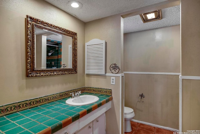 bathroom with tile patterned flooring, vanity, toilet, and a textured ceiling