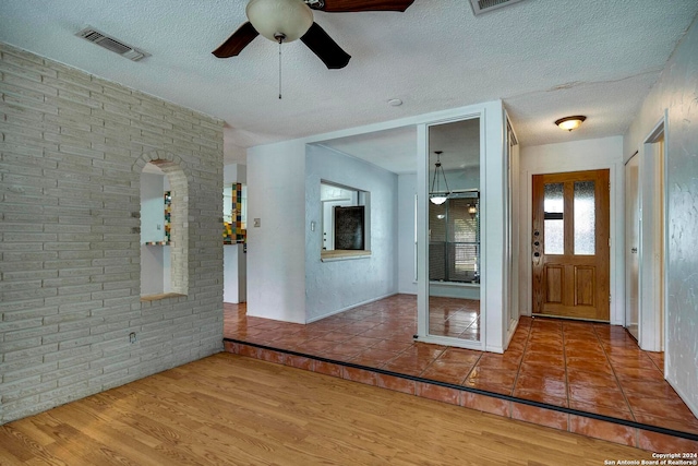 foyer entrance featuring ceiling fan, brick wall, a textured ceiling, and hardwood / wood-style flooring