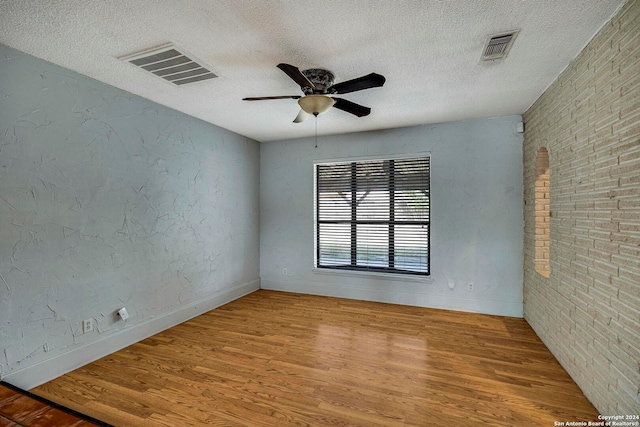 unfurnished room featuring wood-type flooring, a textured ceiling, ceiling fan, and brick wall