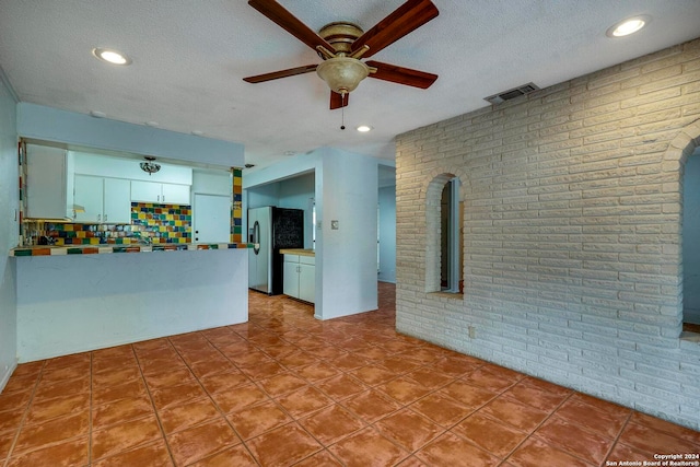 unfurnished living room featuring ceiling fan, brick wall, and a textured ceiling