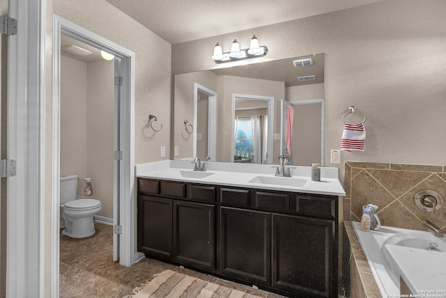 bathroom featuring tiled bath, vanity, a textured ceiling, and toilet