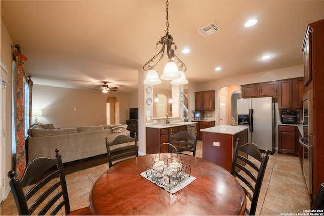 dining space with light tile patterned floors, ceiling fan with notable chandelier, and sink