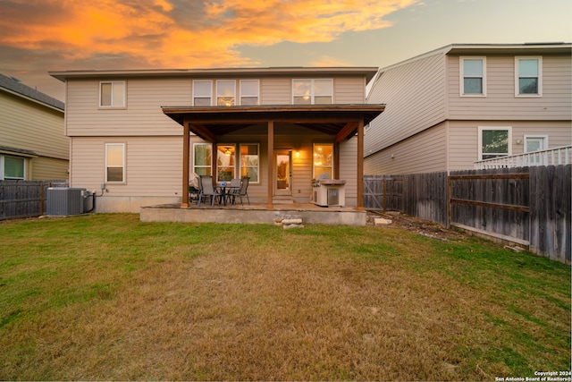 back house at dusk with a yard, a patio, and central AC unit