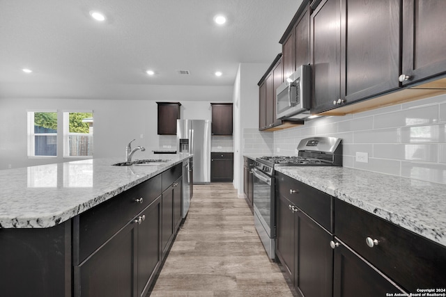 kitchen featuring backsplash, a kitchen island with sink, sink, light hardwood / wood-style flooring, and appliances with stainless steel finishes